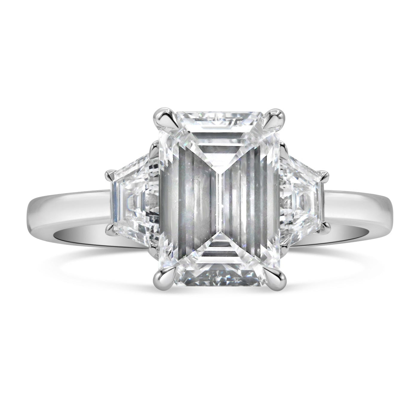 14K white gold three stone ring featuring a lab grown emerald cut center diamond with step cut trapezoid side diamonds.